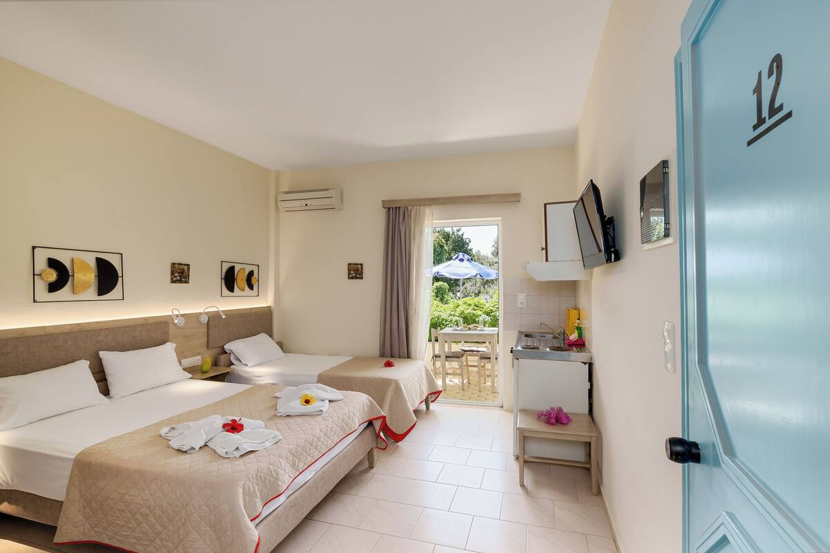 Une chambre d’hôtel avec deux lits, un bureau, une chaise et une vue sur le jardin depuis la porte.