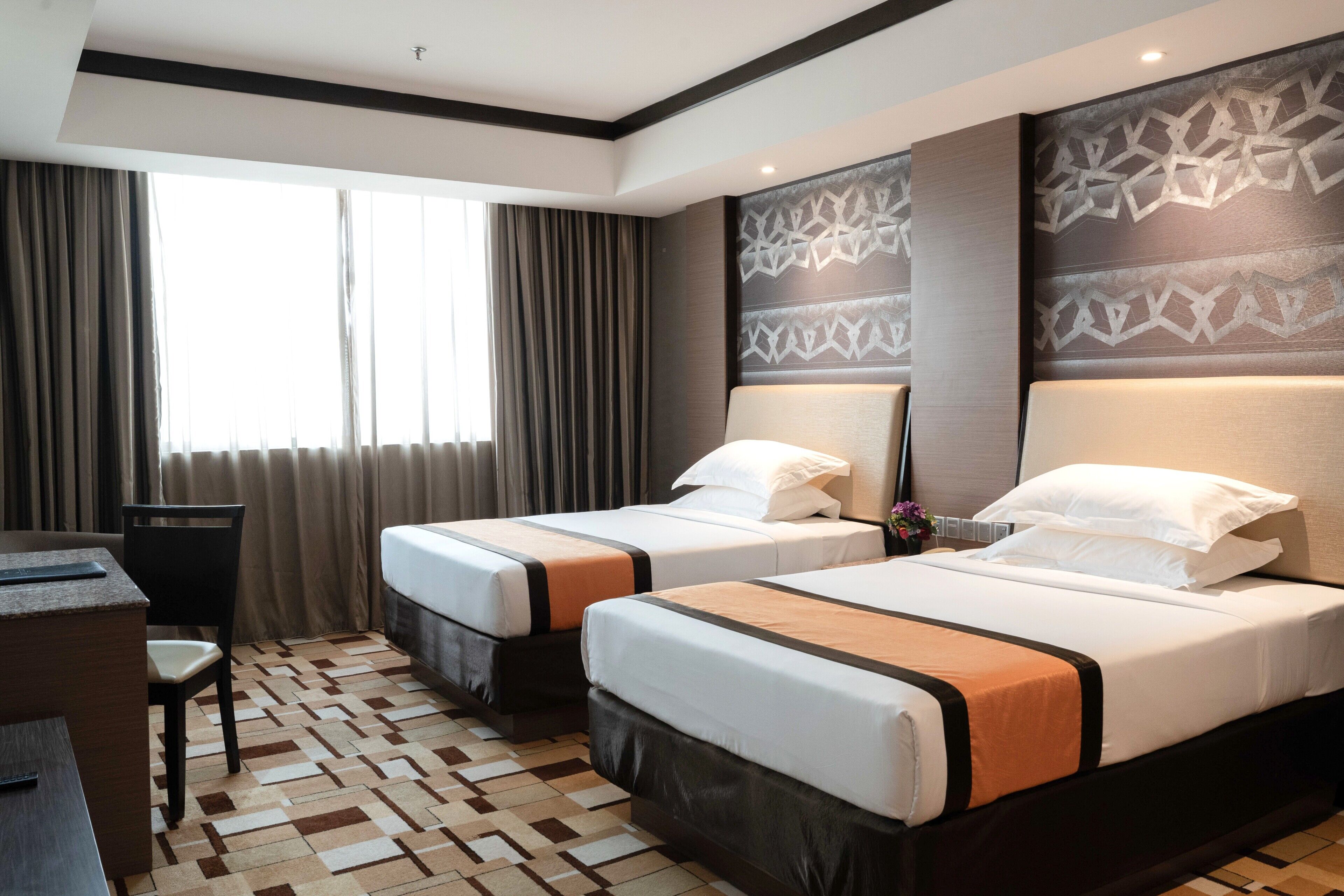 A hotel room with two beds, a desk, and a patterned carpet.
