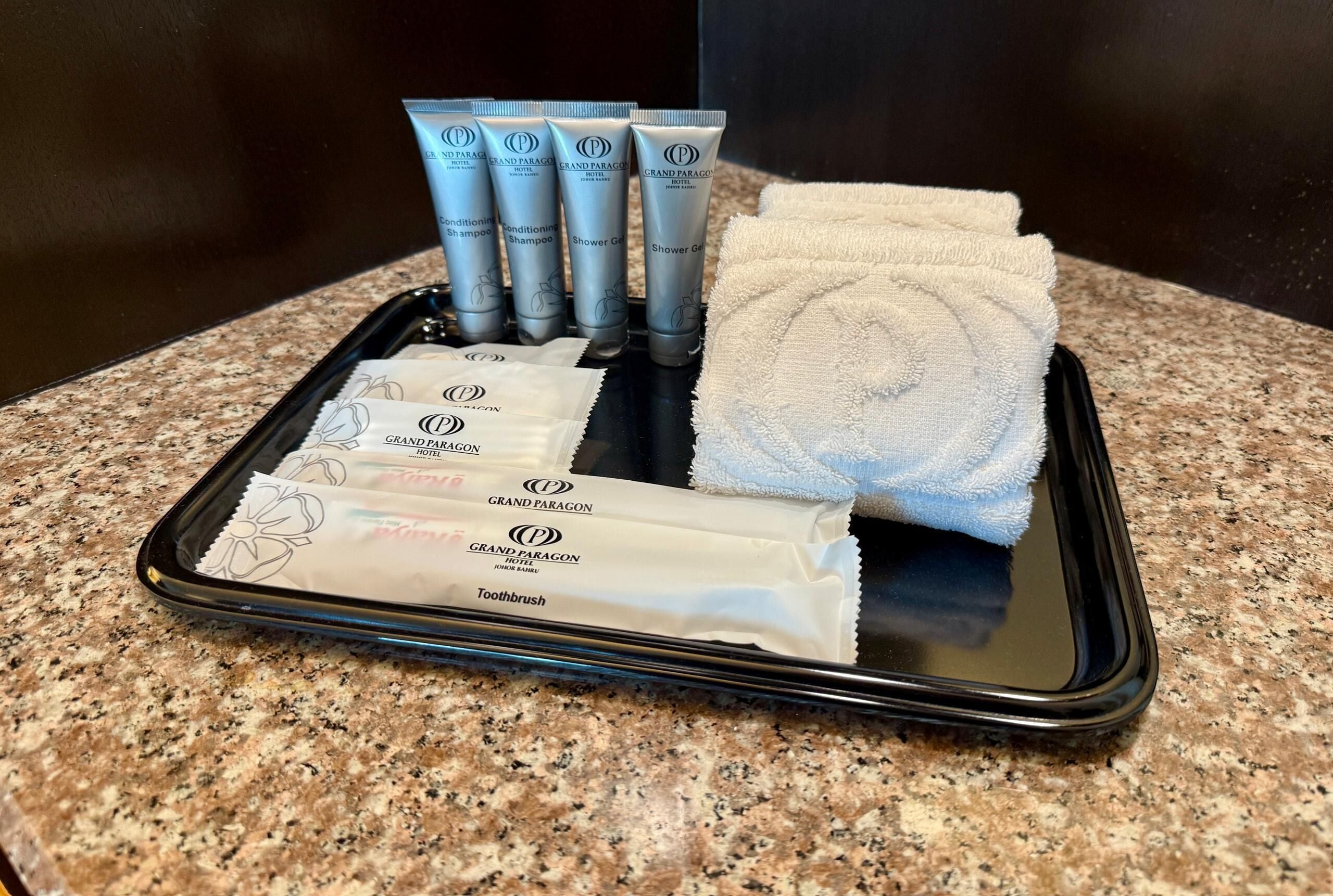Un plateau contenant des articles de toilette, notamment une brosse à dents, du shampoing, un après-shampoing et du gel douche.
