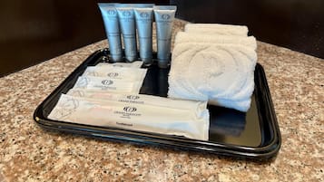 Un vassoio con articoli da toilette, tra cui shampoo, balsamo, bagnoschiuma e uno spazzolino, insieme a un asciugamano piegato.