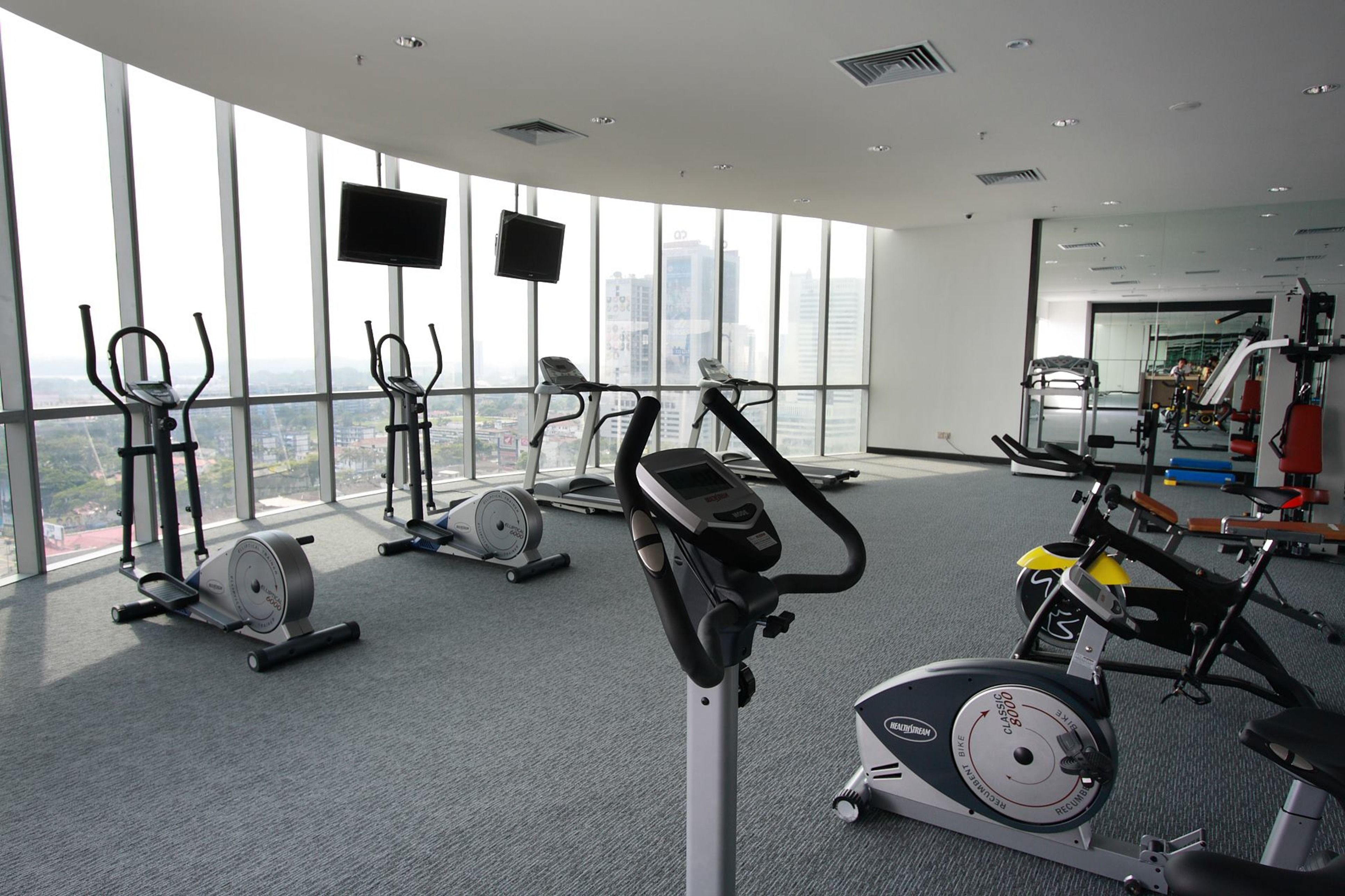 A gym with various exercise equipment, large windows, and a view of the city.