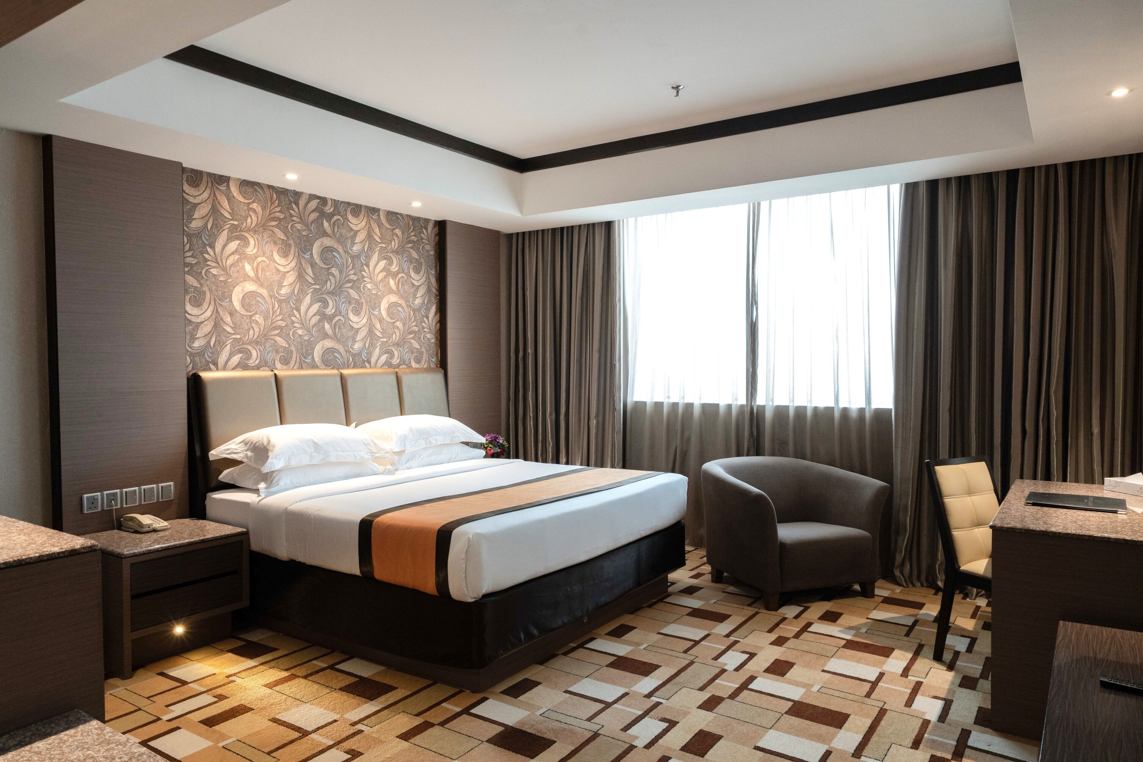 A hotel room with a large bed, a desk, a chair, and a window with curtains.