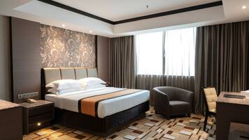 A hotel room with a large bed, a desk, a chair, and a window with curtains.
