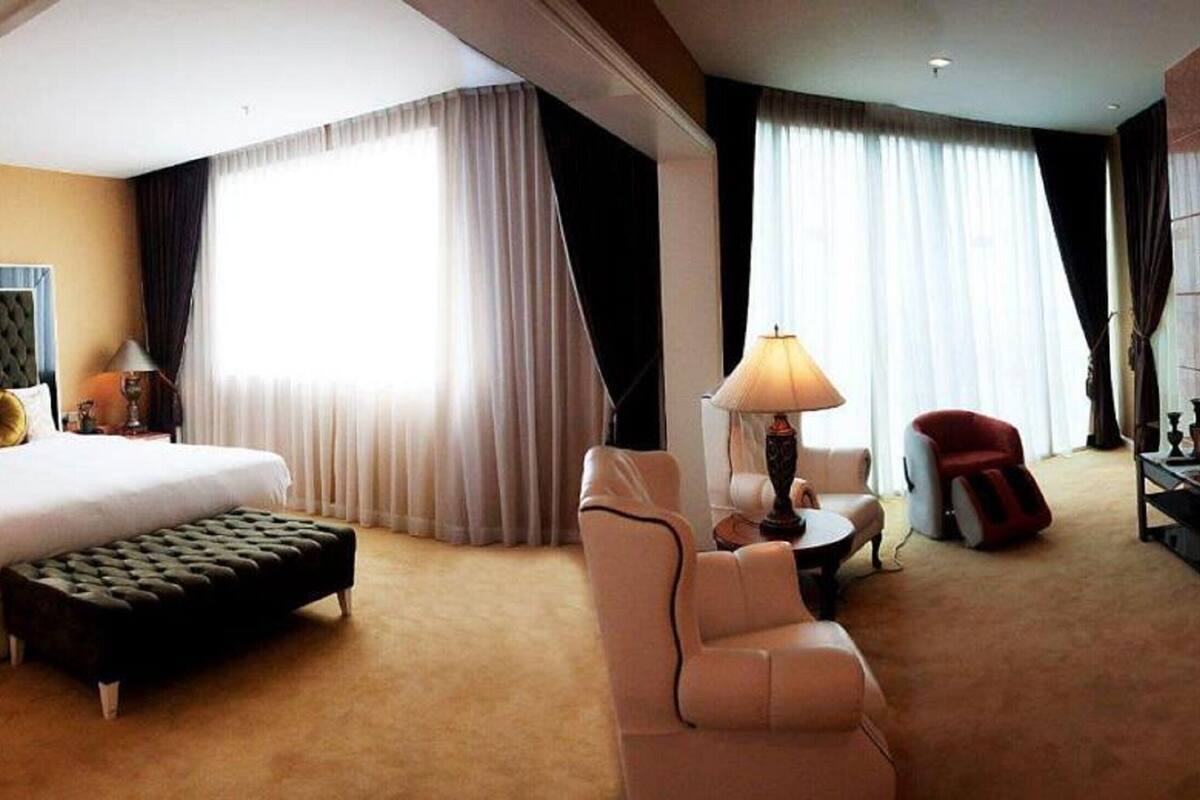 Une chambre d’hôtel avec un grand lit, un coin salon avec une lampe, une télévision et un fauteuil rouge.