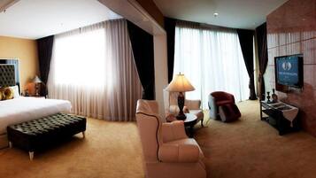 A hotel room with a large bed, a sitting area with a lamp, a television, and a red chair.