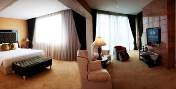 A hotel room with a large bed, a sitting area with a lamp, a television, and a red chair.