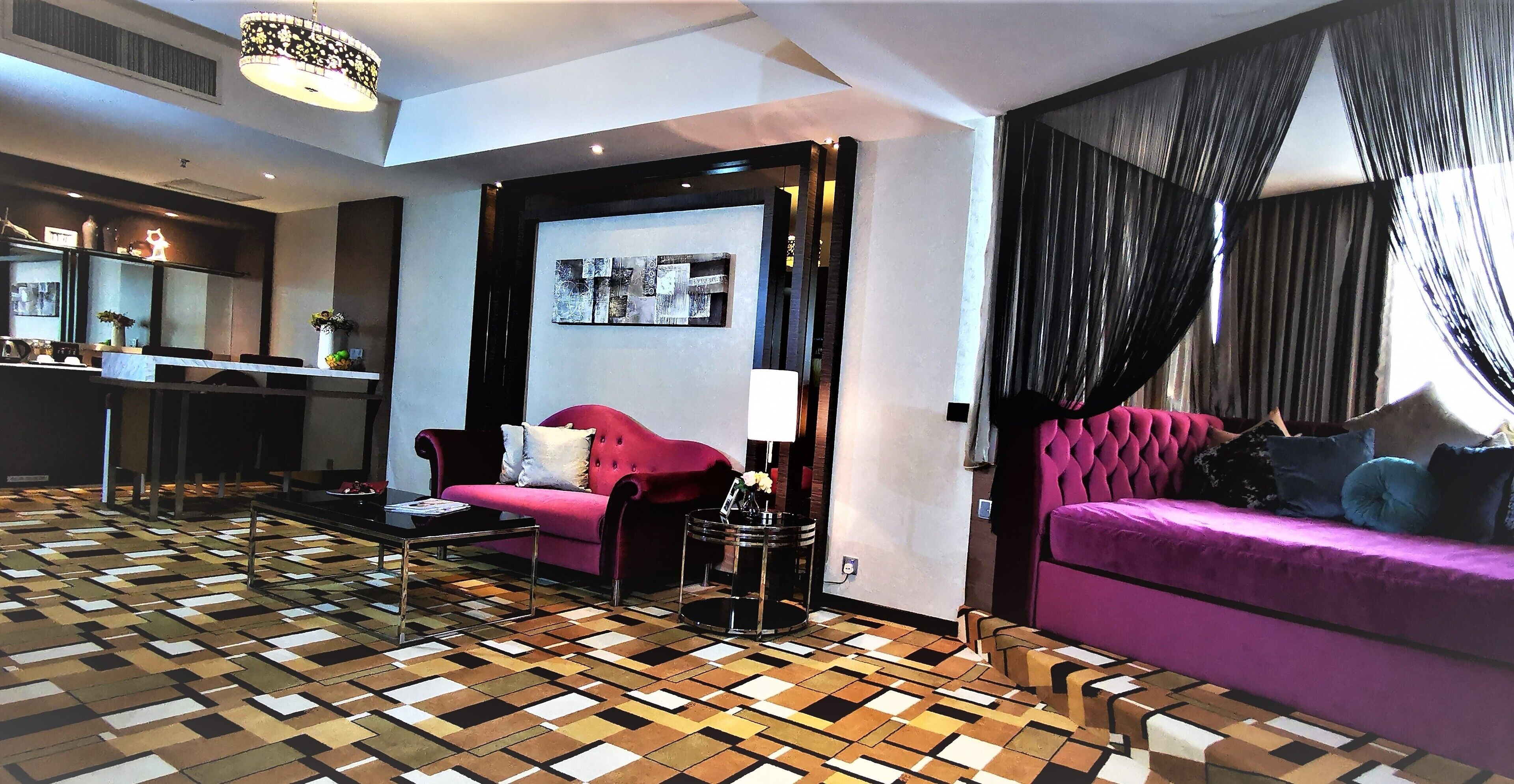 Una sala de estar moderna con piso estampado, un sofá rojo, un sofá morado y un comedor con mesa de vidrio.
