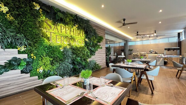 A modern dining area with a green wall, wooden tables, and chairs. - Grand Paragon Hotel Johor Bahru (Johor Bahru)