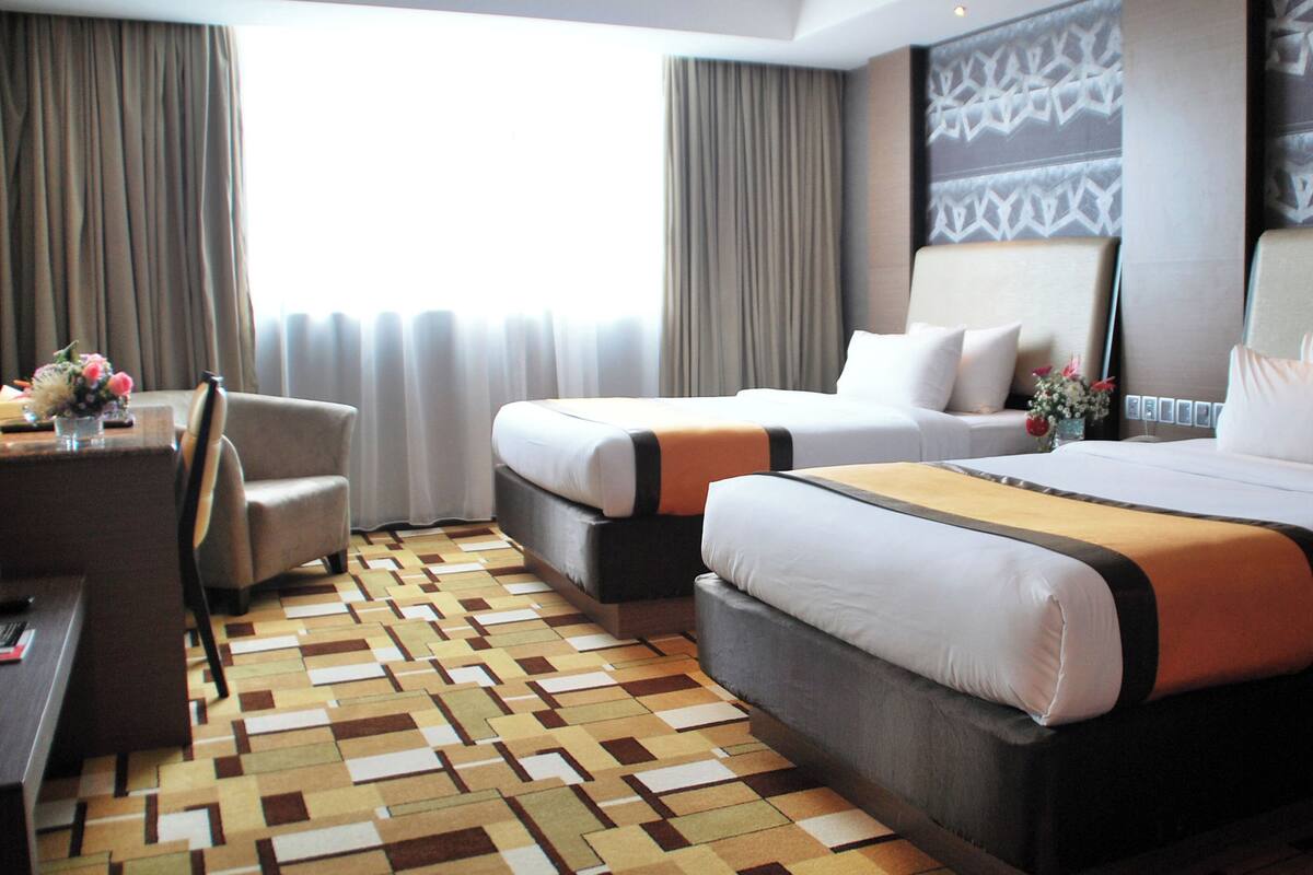 Une chambre d’hôtel avec deux lits, un bureau, une chaise et une moquette à motifs.