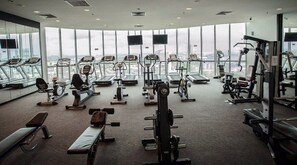Ein Fitnessstudio mit Laufbändern, Kraftgeräten und Bänken, große Fenster mit Blick auf die Stadt.