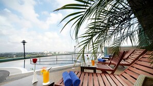 A rooftop terrace with wooden lounge chairs, a table with a drink and a rose, and a view of the cityscape. - Grand Paragon Hotel Johor Bahru (Johor Bahru)