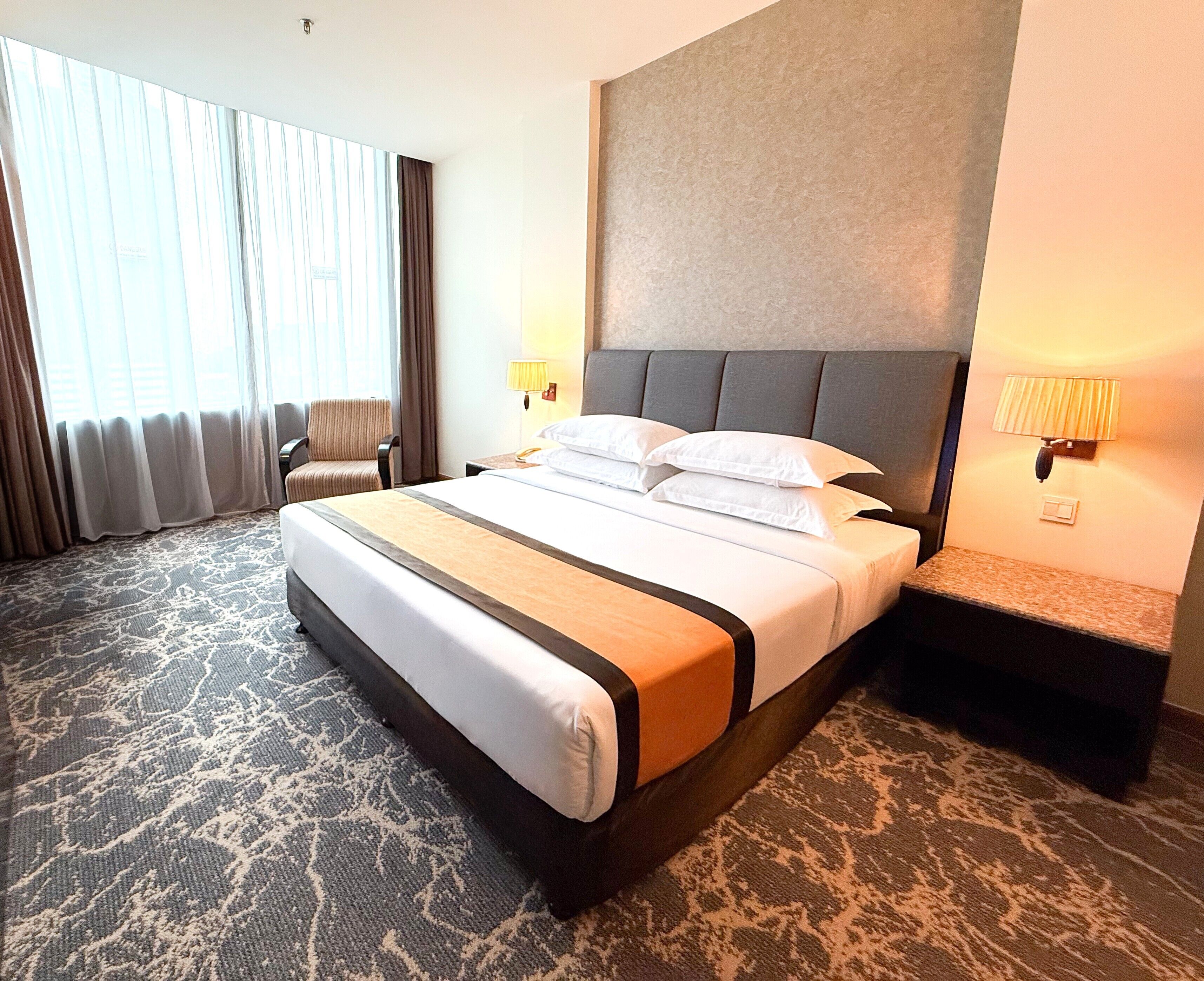A hotel room with a large bed, a chair, a nightstand, and a lamp.