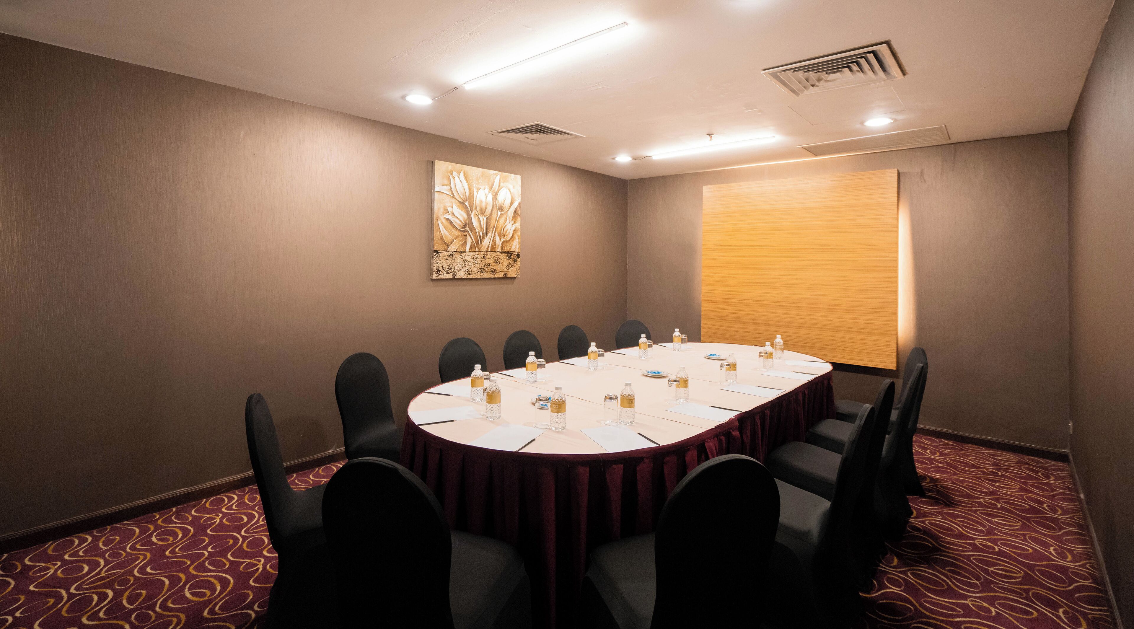 A conference room with a round table, black chairs, water bottles, and a large abstract painting on the wall.