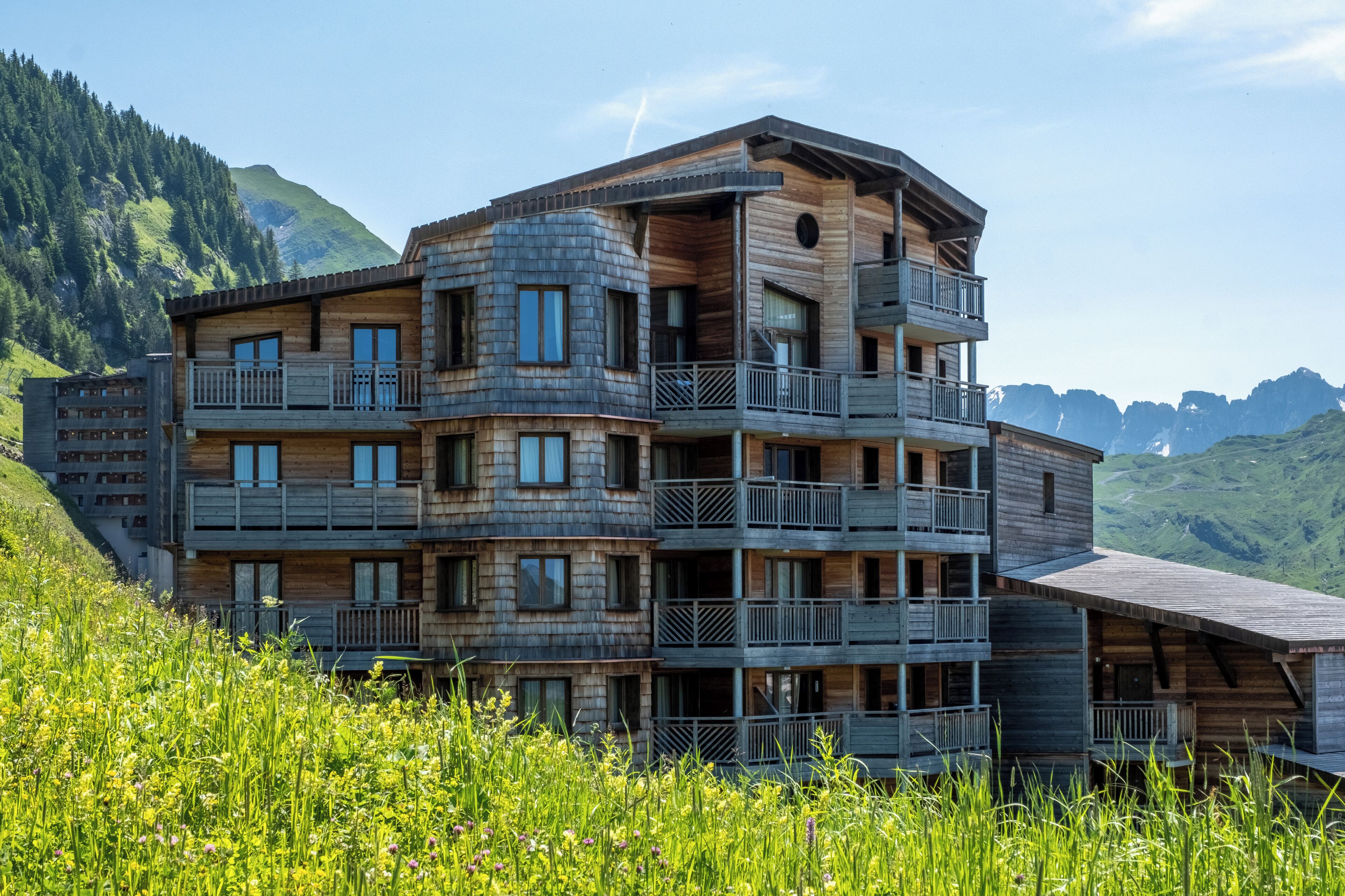 A multi-story wooden building with balconies, set against a mountainous backdrop.