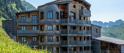 A multi-story wooden building with balconies, set against a mountainous backdrop.
