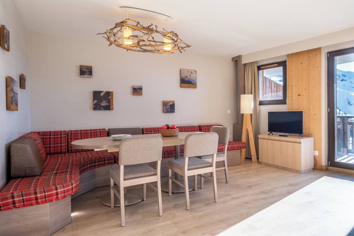 Una sala moderna con un sofá seccional, una mesa de comedor redonda, sillas, un televisor y obras de arte en las paredes.