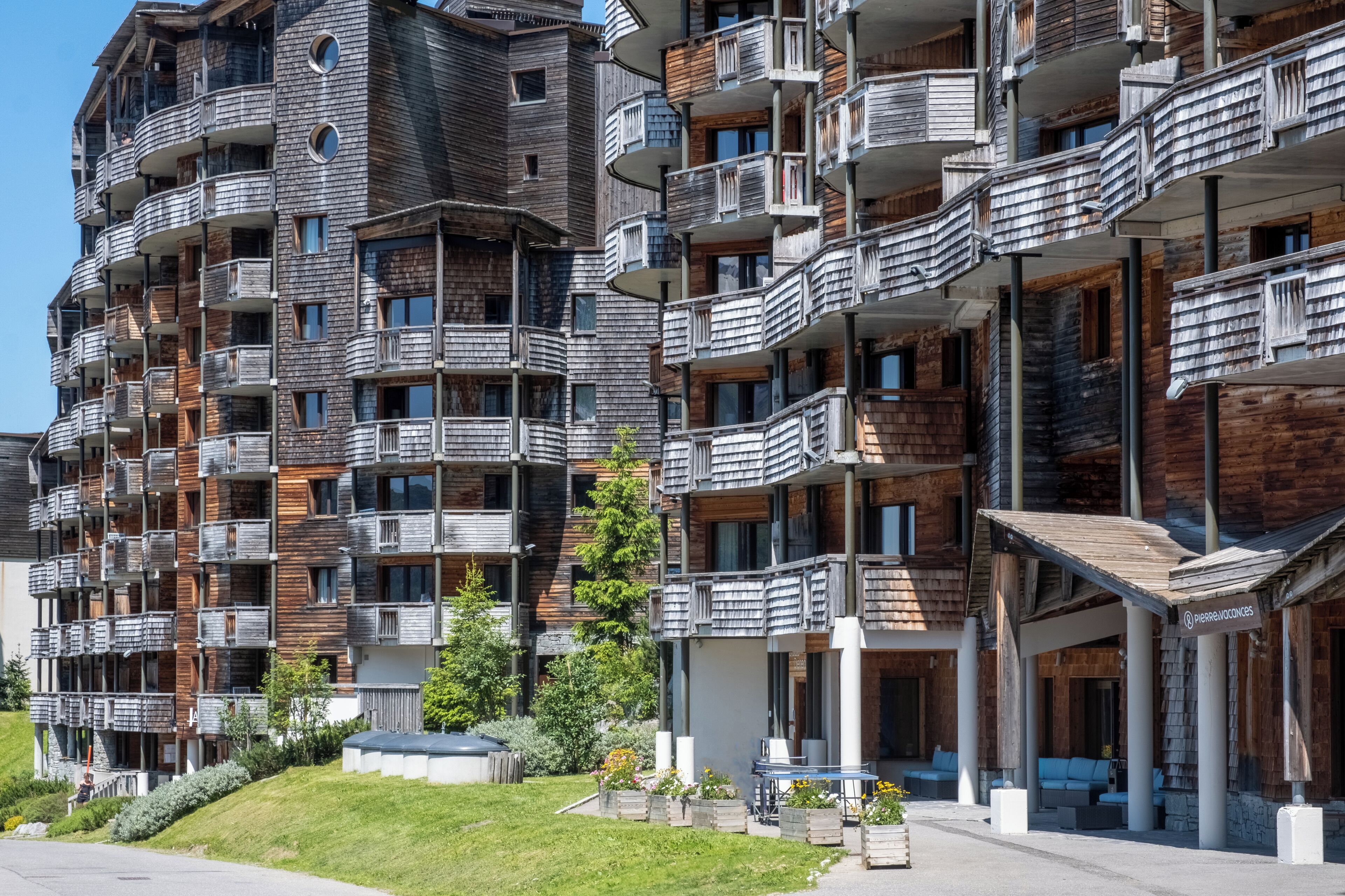 Un edificio de varios pisos con balcones, una zona de estar al aire libre techada y un patio con césped.