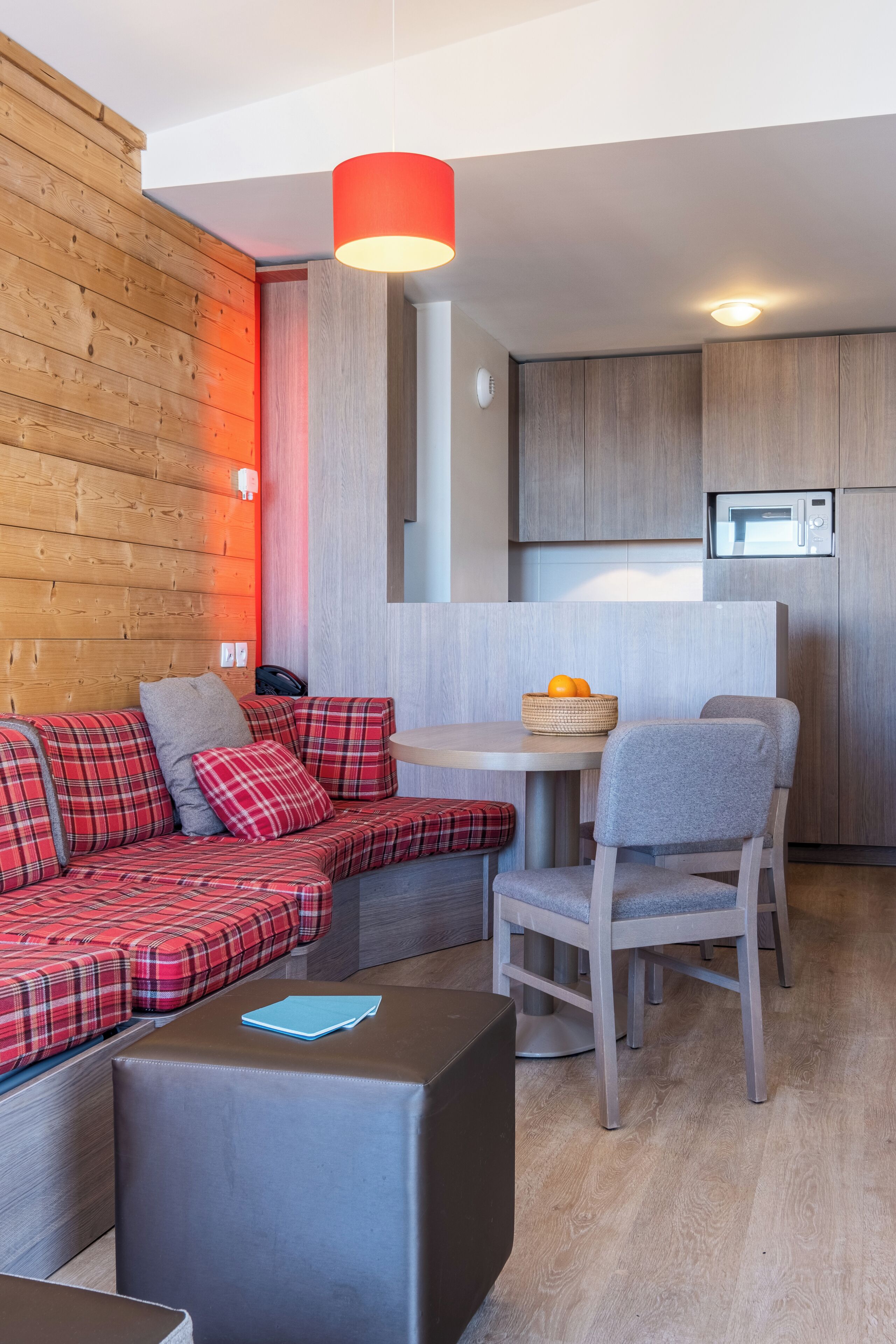 Une cuisine moderne et fonctionnelle équipée d’un four à micro-ondes, un coin repas avec une table et des chaises, et un canapé rouge à carreaux agrémenté de coussins.