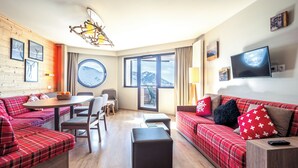 A modern living room with a sofa, ottoman, dining table, chairs, and a TV. - Résidence Pierre & Vacances Atria Crozats (Avoriaz)