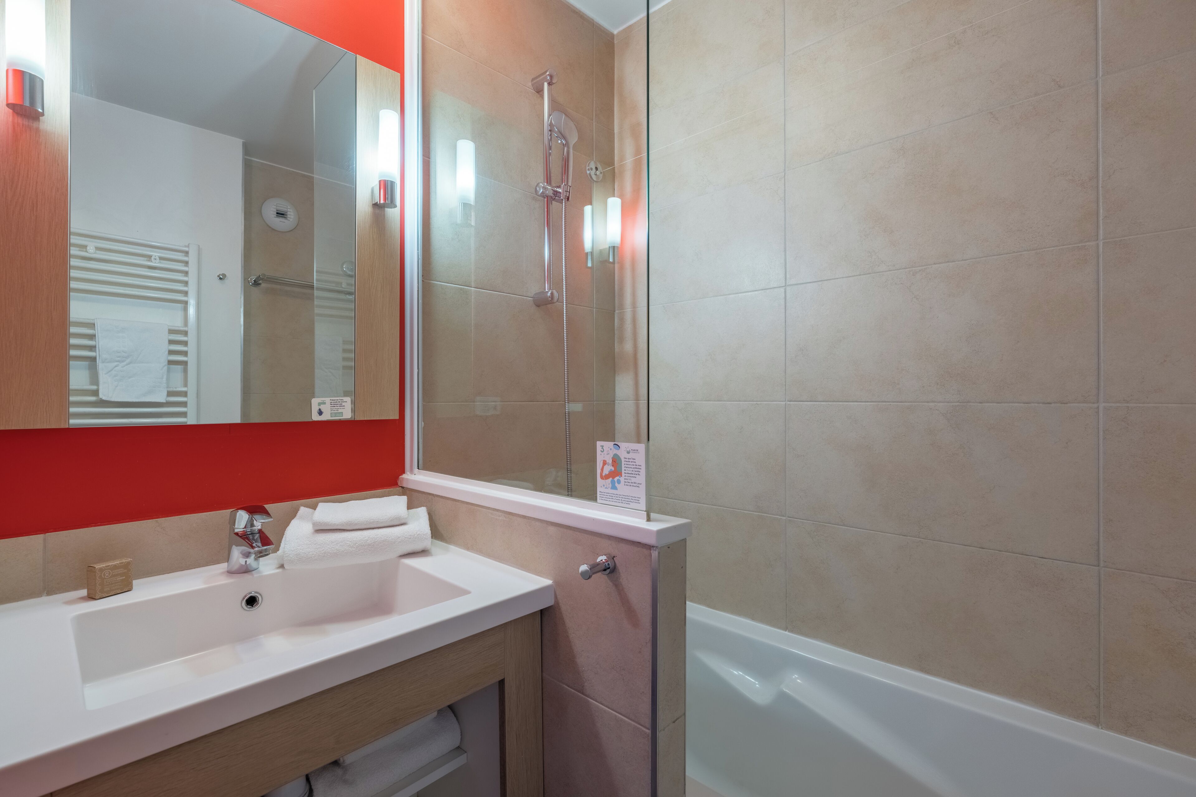 A bathroom with a white sink, a mirror, a shower, and beige tiles.