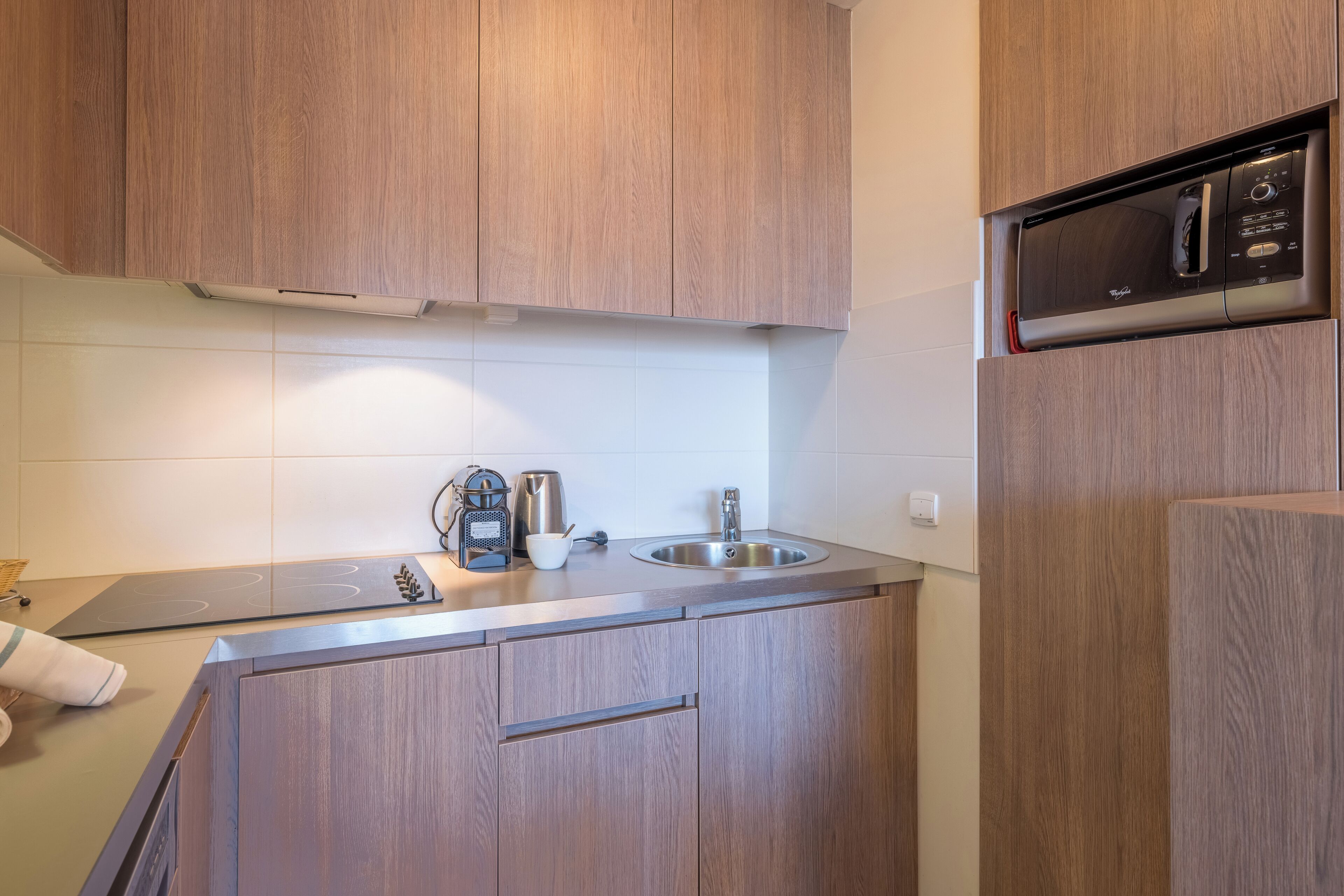 A compact kitchen with wooden cabinets, a stainless steel sink, a microwave, and a kettle.