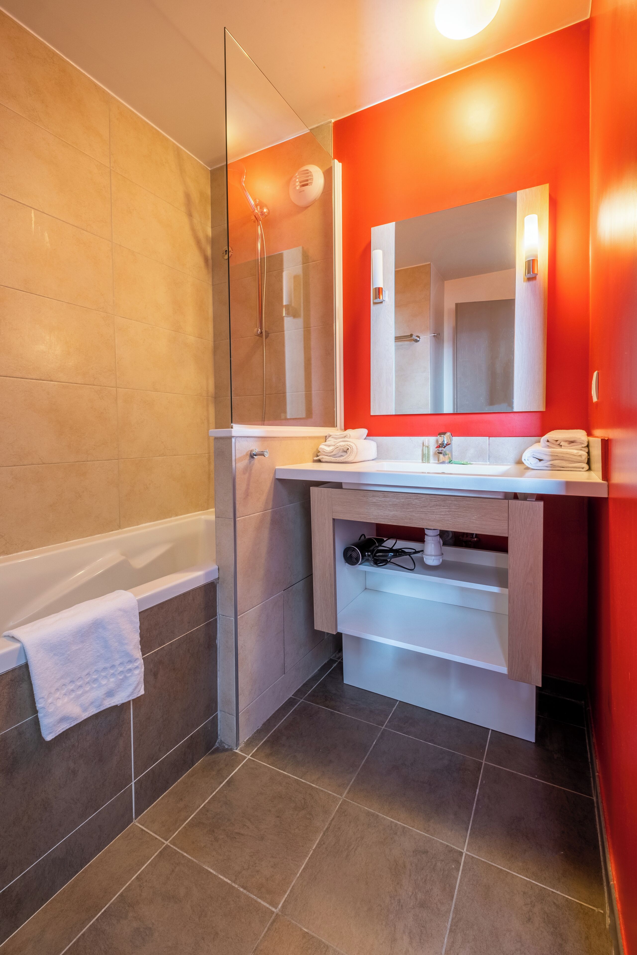 A modern bathroom with a glass shower enclosure, a white bathtub, a vanity with a mirror, and a red accent wall.