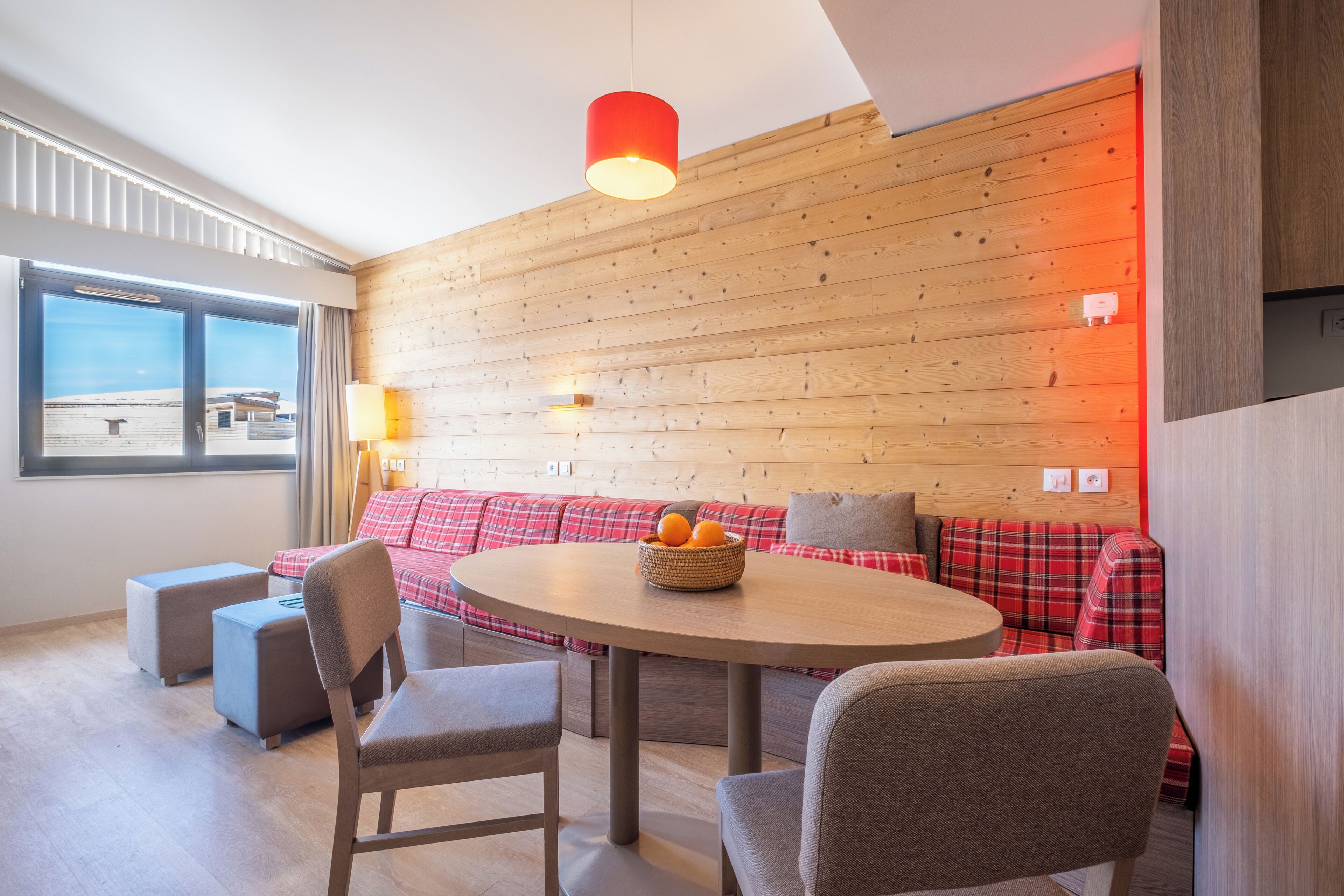 A modern room with a wooden wall, a round table, and a red plaid sofa.