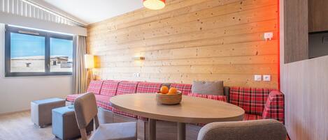A modern room with a wooden wall, a round table, and a red plaid sofa.