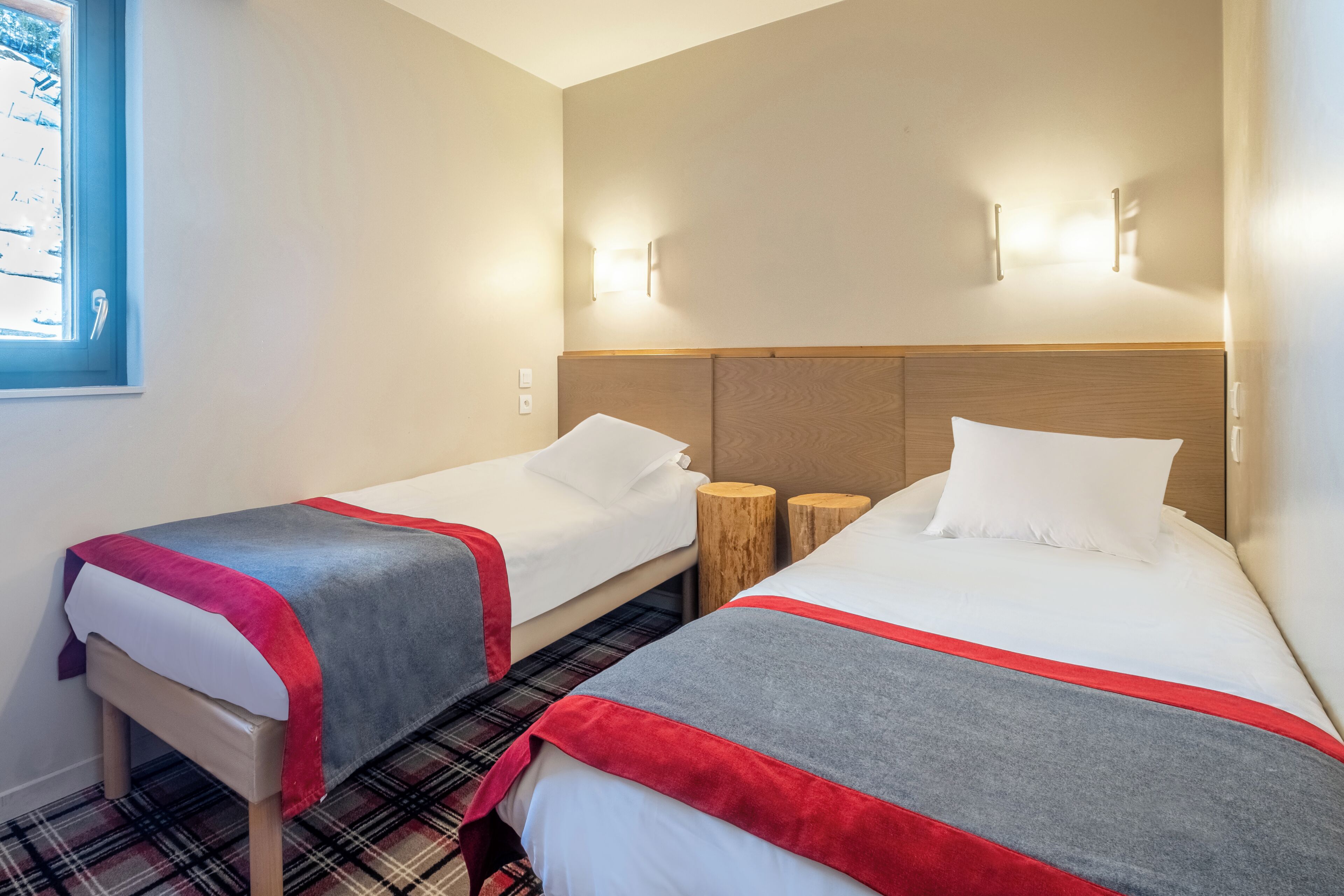 Une chambre d’hôtel avec deux lits, une fenêtre et un luminaire fixé au mur.