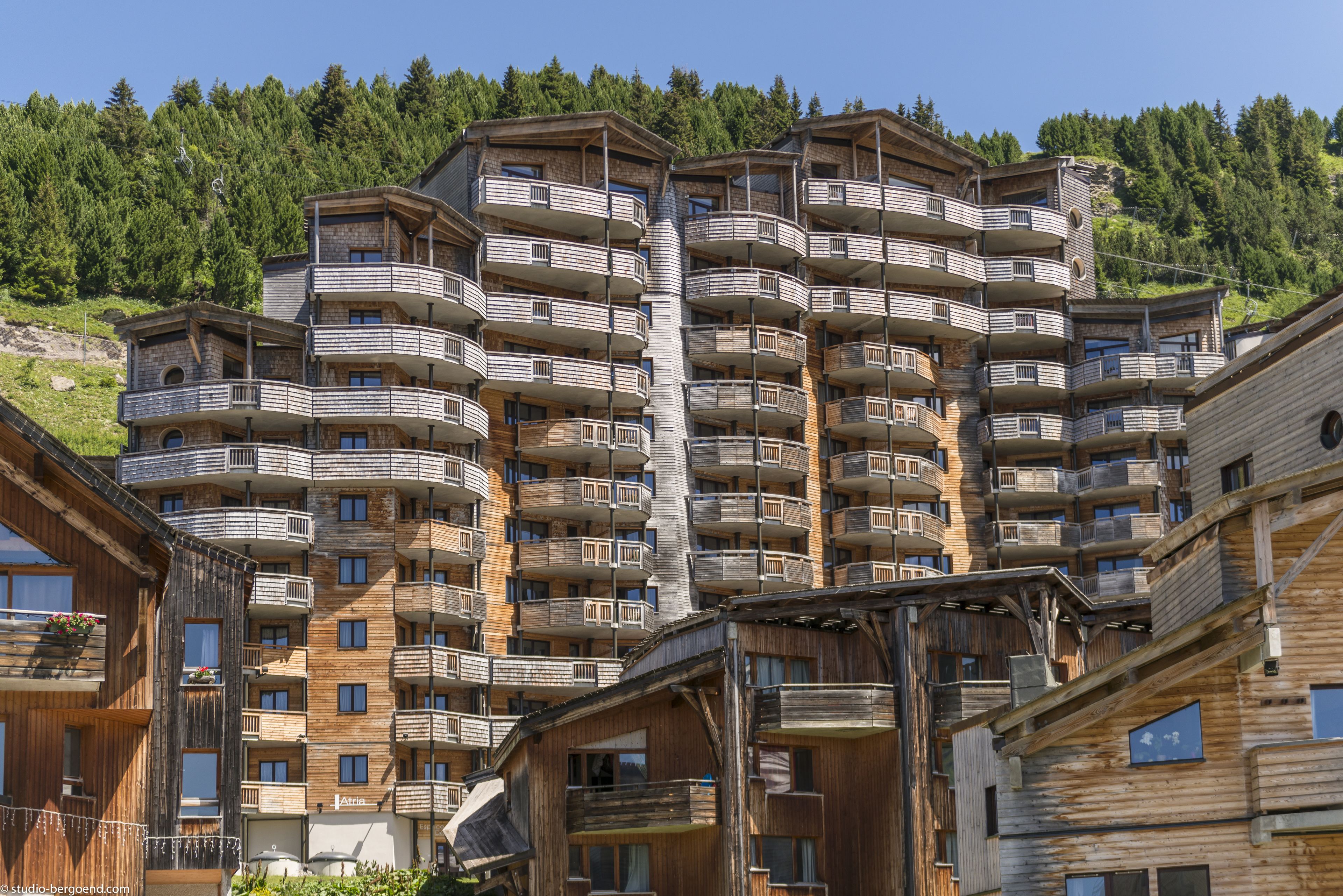 Een hotel met meerdere verdiepingen, balkons, een houten gevel en een bergachtige achtergrond.