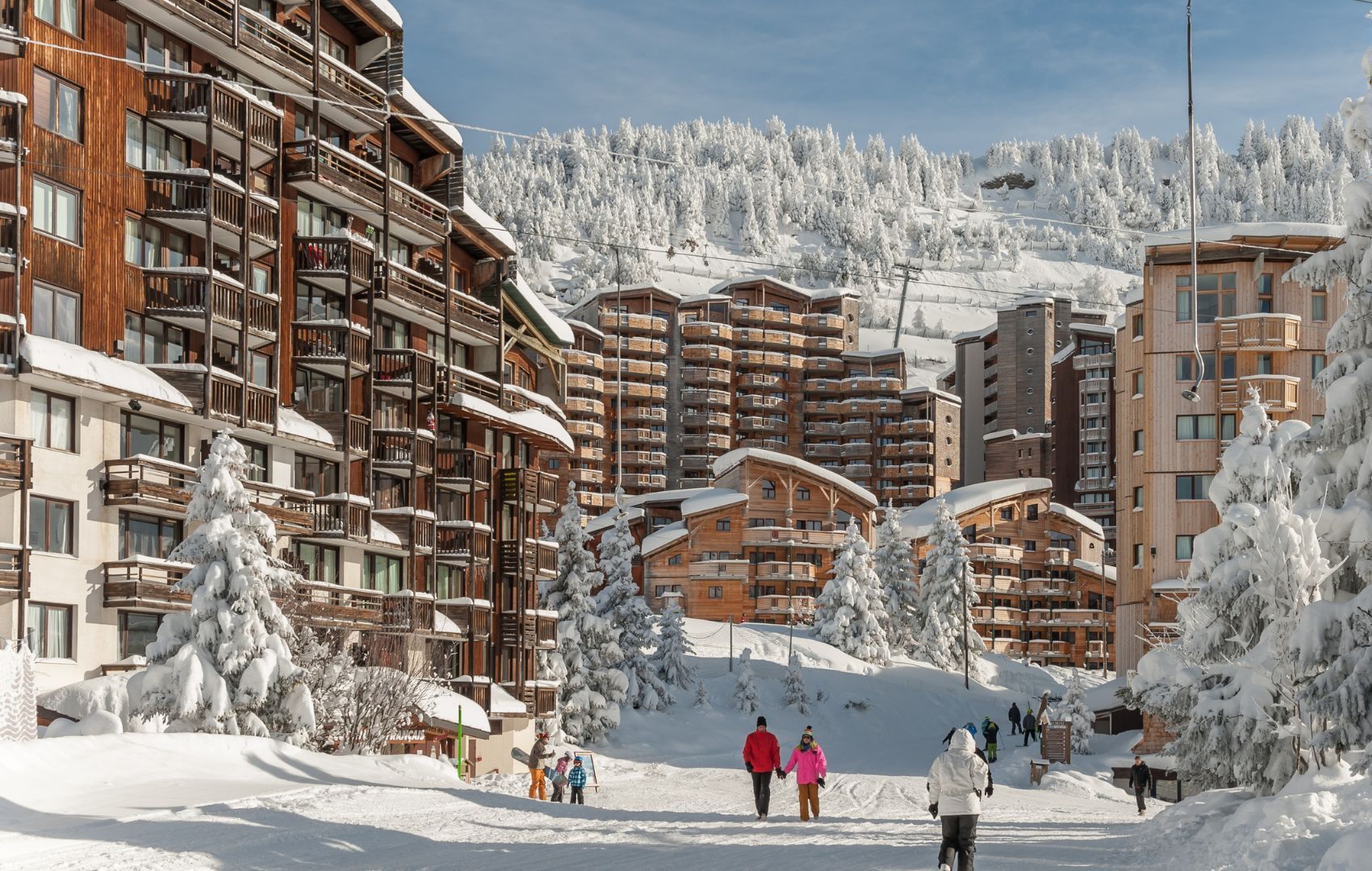 Estância de esqui coberta de neve com edifícios altos, pistas de esqui e árvores carregadas de neve.