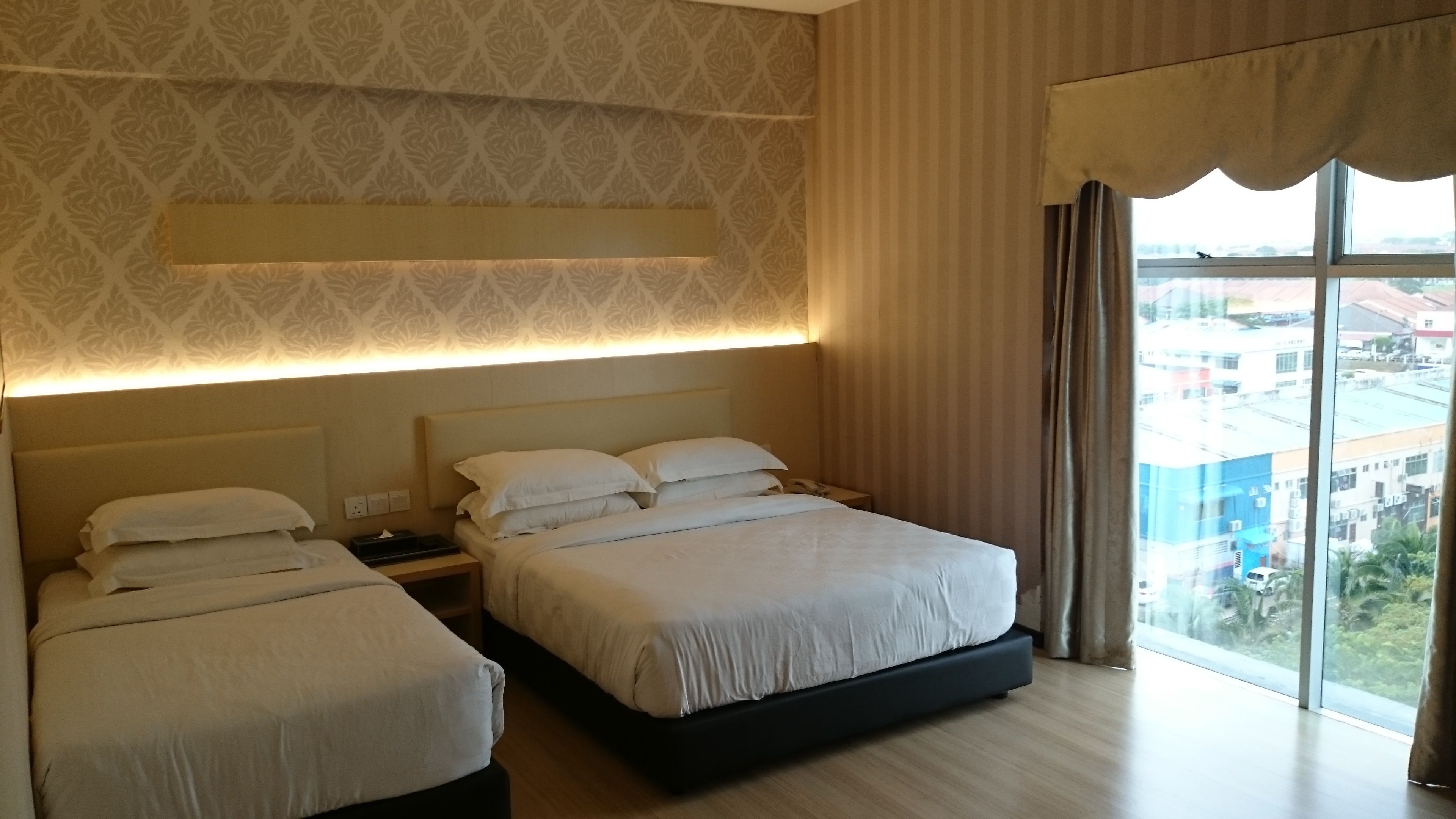 A hotel room with two beds, a large window with curtains, and a patterned wallpaper.