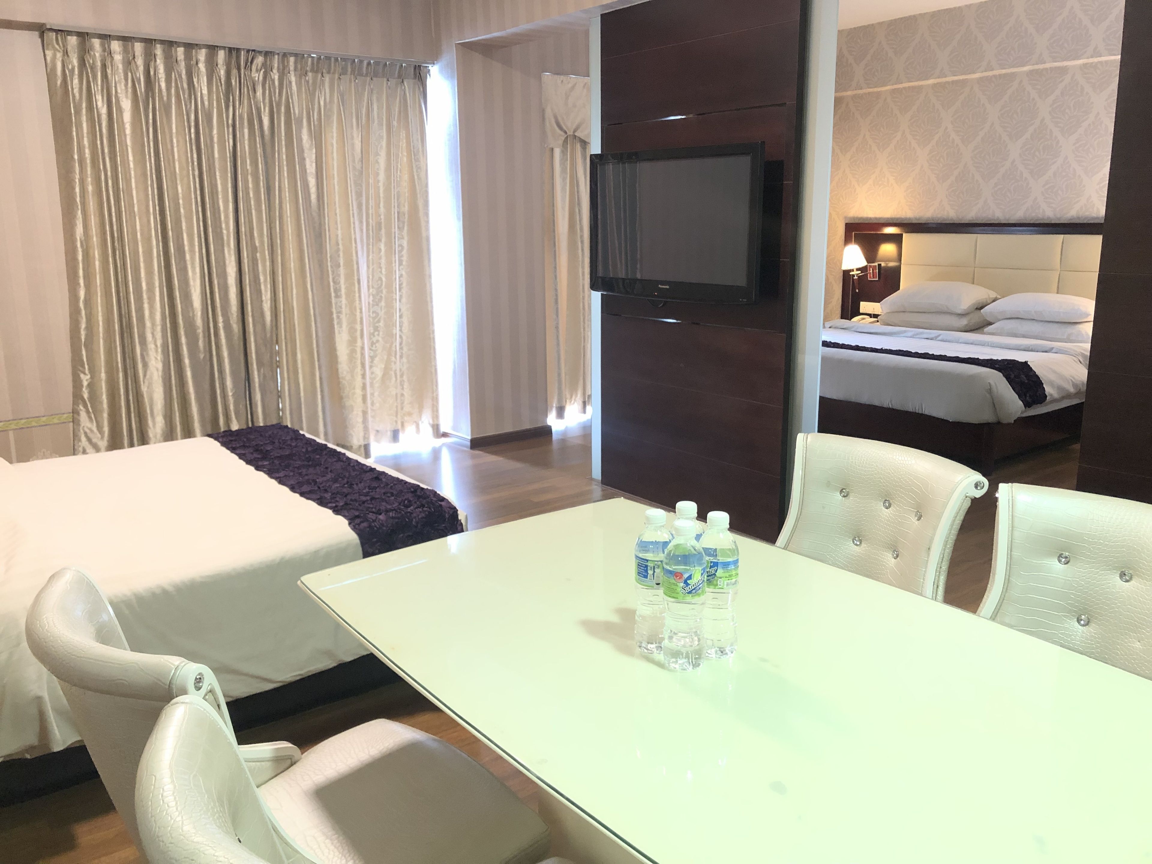 Habitación de hotel con dos camas, un televisor montado en la pared, una mesa con botellas de agua y una lámpara en la mesita de noche.