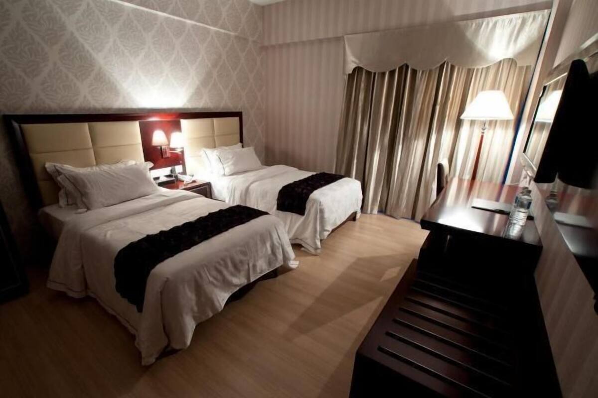 A hotel room with two beds, a desk, a chair, a lamp, and a window with curtains.