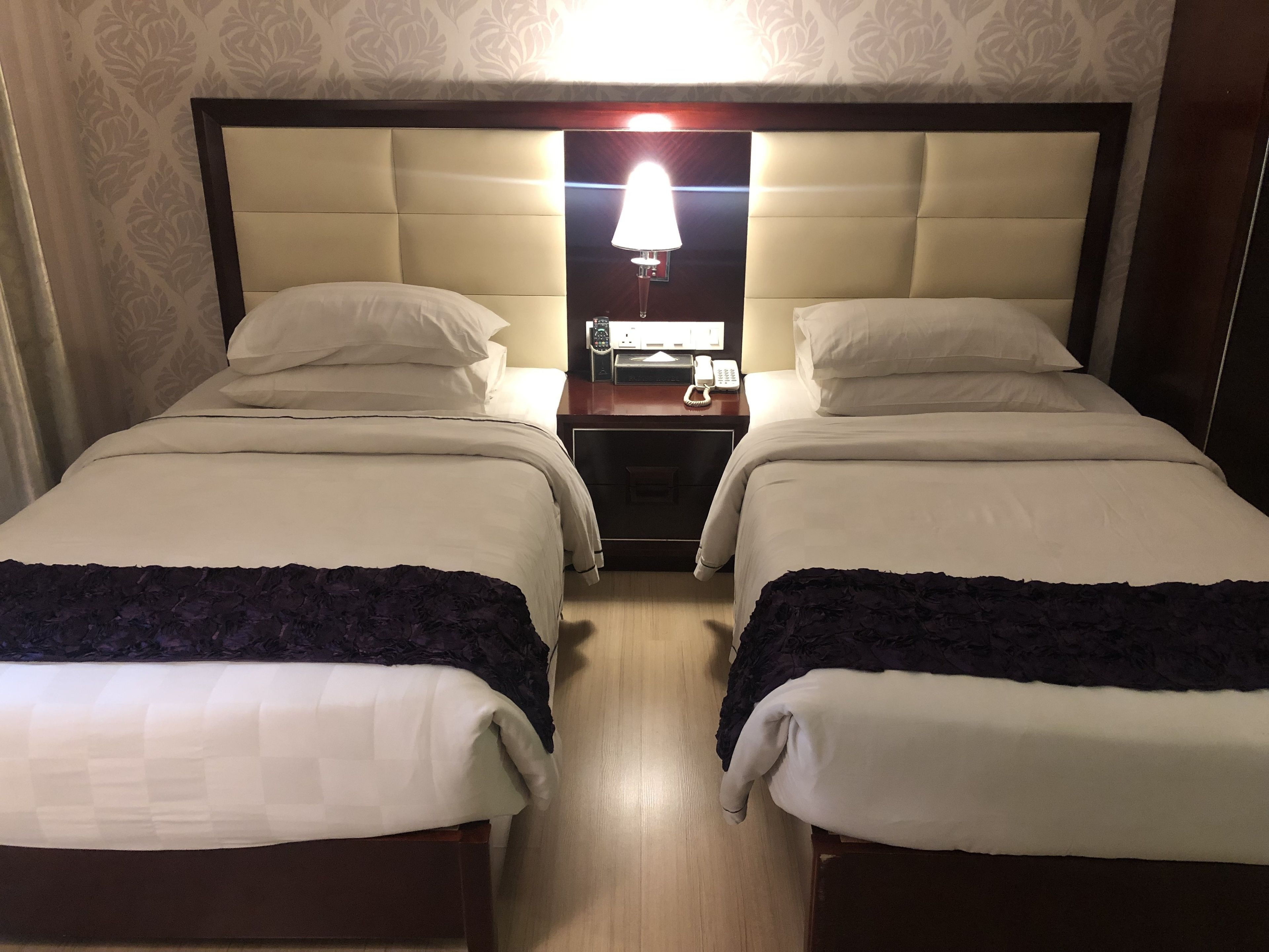 Hotelkamer met twee bedden, elk voorzien van een hoofdeinde, nachtkastje met lamp en telefoon.