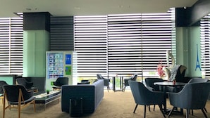 Un área de descanso moderna con máquinas expendedoras, asientos y ventanas amplias con persianas.