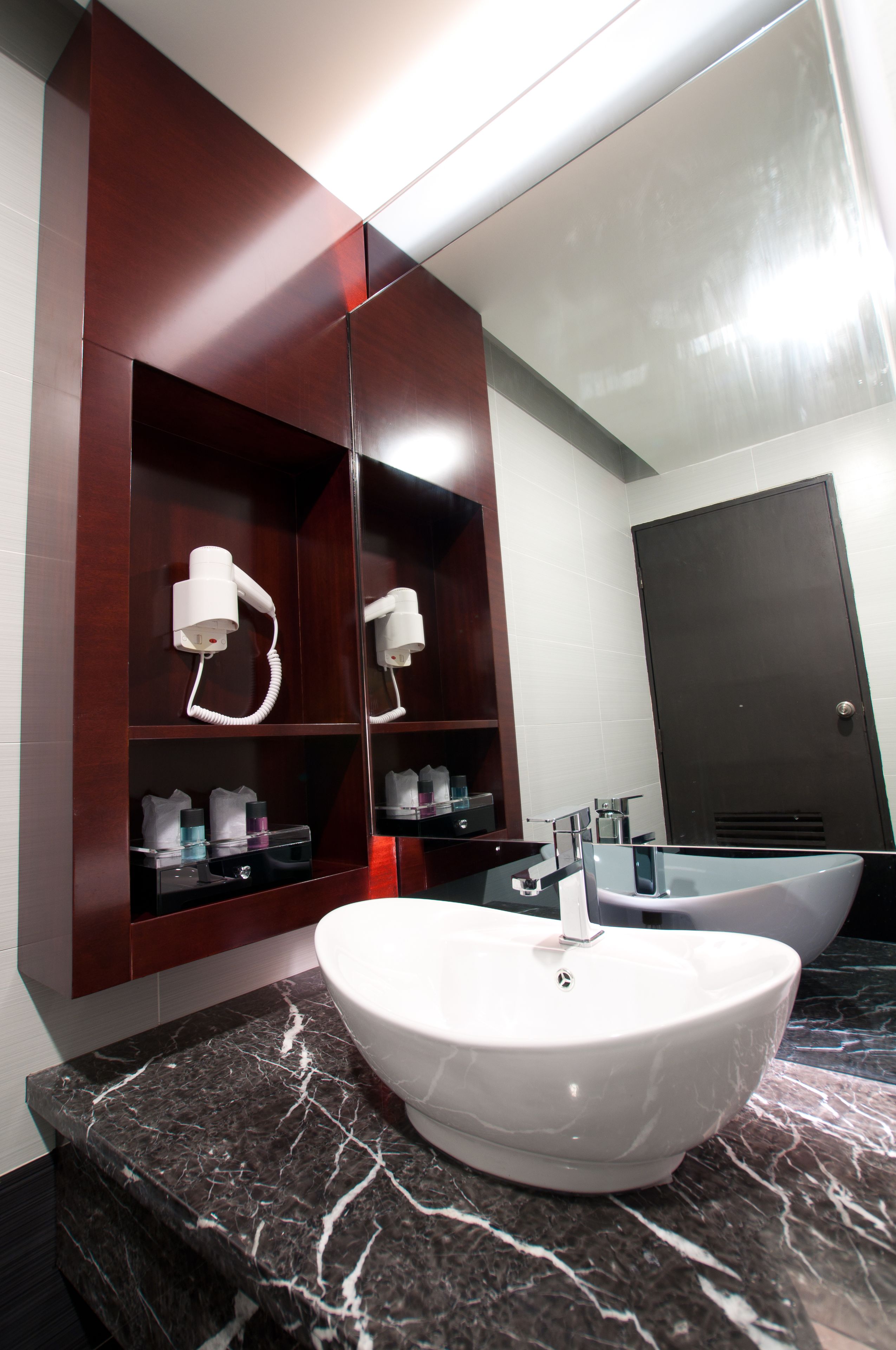 A modern bathroom with a large mirror, a white sink, and a dark wooden vanity with a hairdryer.