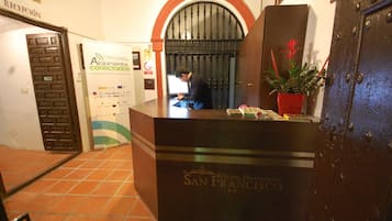 A reception desk at Hotel Hospedero San Francisco with a tiled floor, a potted plant, and a large metal door.