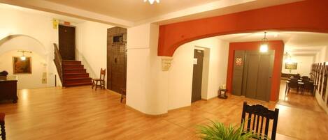 A spacious lobby with wooden flooring, a staircase, and a chandelier.