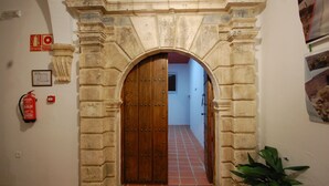 Arc de pedra que dona a una estança amb sòl de rajola i una porta de fusta.