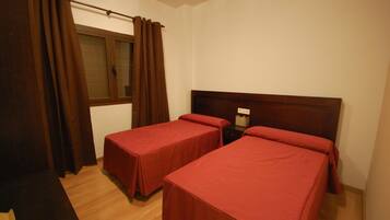 Una habitación con dos camas individuales, una ventana con cortinas, una mesita de noche con lámpara y suelo de madera.