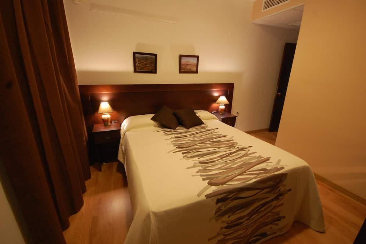 A hotel room with a bed, two bedside lamps, and two framed pictures on the wall.
