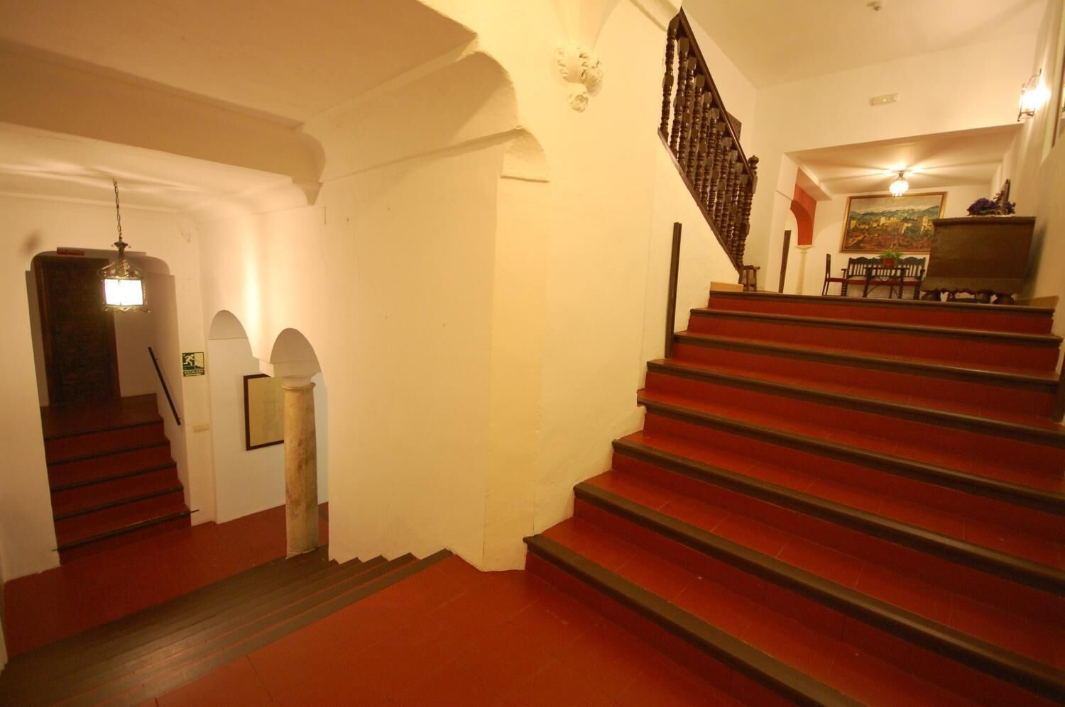 Eine Treppe mit roten Stufen führt zu einer Zwischenebene mit einem Holzgeländer und einer Leuchte darüber.