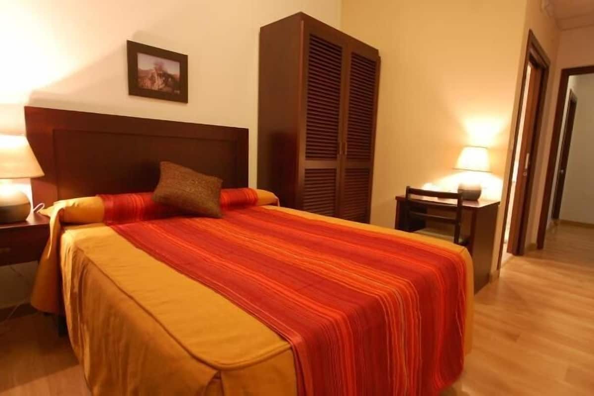 A hotel room with a bed, two bedside tables, a nightstand, a wardrobe, and a door.