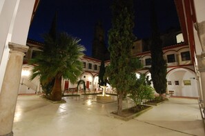A courtyard with palm trees, a fountain, and a building with arches and columns. - Hospedería San Francisco (Priego de Córdoba)
