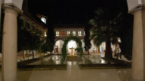 Un pati amb una font, palmeres i un edifici d'arcs i columnes.