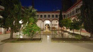 Un pati amb una font, palmeres i un edifici amb finestres d'arc i un teulat vermell.