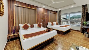 Habitación de hotel con dos camas, ventilador de techo, ventana grande con vistas y suelo de madera.