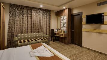 A hotel room with a bed, a sofa, a TV, and a small desk with a mirror and a shelf.