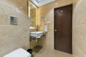 A bathroom with a marble wall, a sink, a mirror, and a door. - The Royal Melange Beacon (Ajmer)